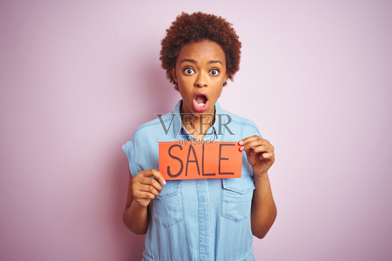 拿着促销板，在粉色背景前震惊的黑人妇女照片摄影图片