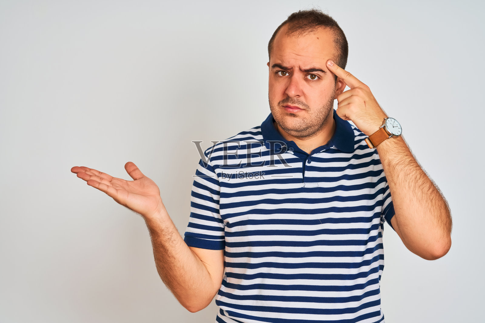 年轻男子穿着休闲条纹马球站在孤立的白色背景困惑和恼火的摊开的手掌显示拷贝空间和指向额头。想想。照片摄影图片