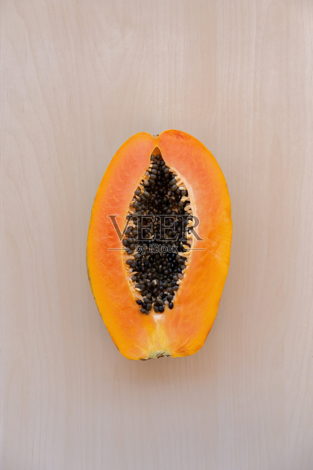 热带番木瓜果实，切成橙色，有黑色的种子，在孤立的木光背景上。生水果是健康食品。饮食。纯素食和素食主义。照片摄影图片
