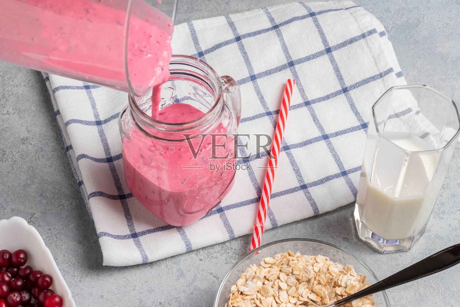 将新鲜自制的酸奶、燕麦片和蔓越莓奶昔倒进杯子里照片摄影图片