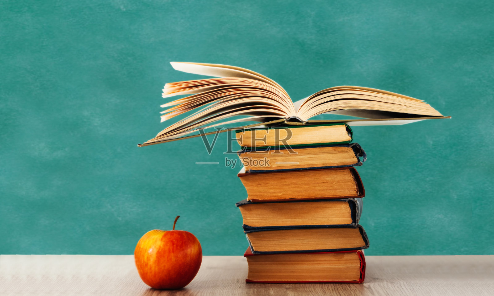 回到学校，堆着书本和苹果用空绿校板作背景，树立教育理念照片摄影图片