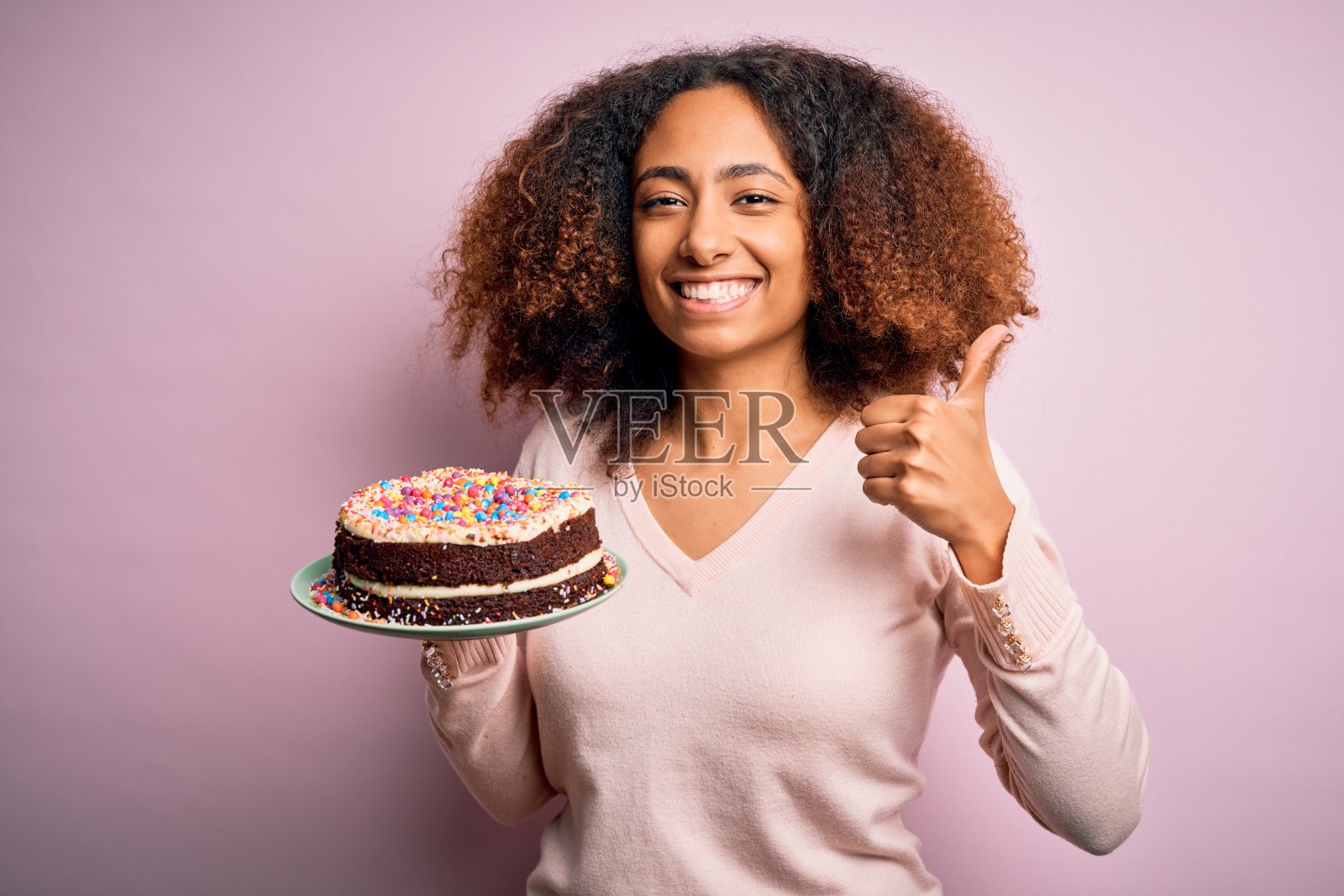 笑容灿烂的非洲裔美国年轻女性手持美味生日蛋糕，比出OK手势照片摄影图片