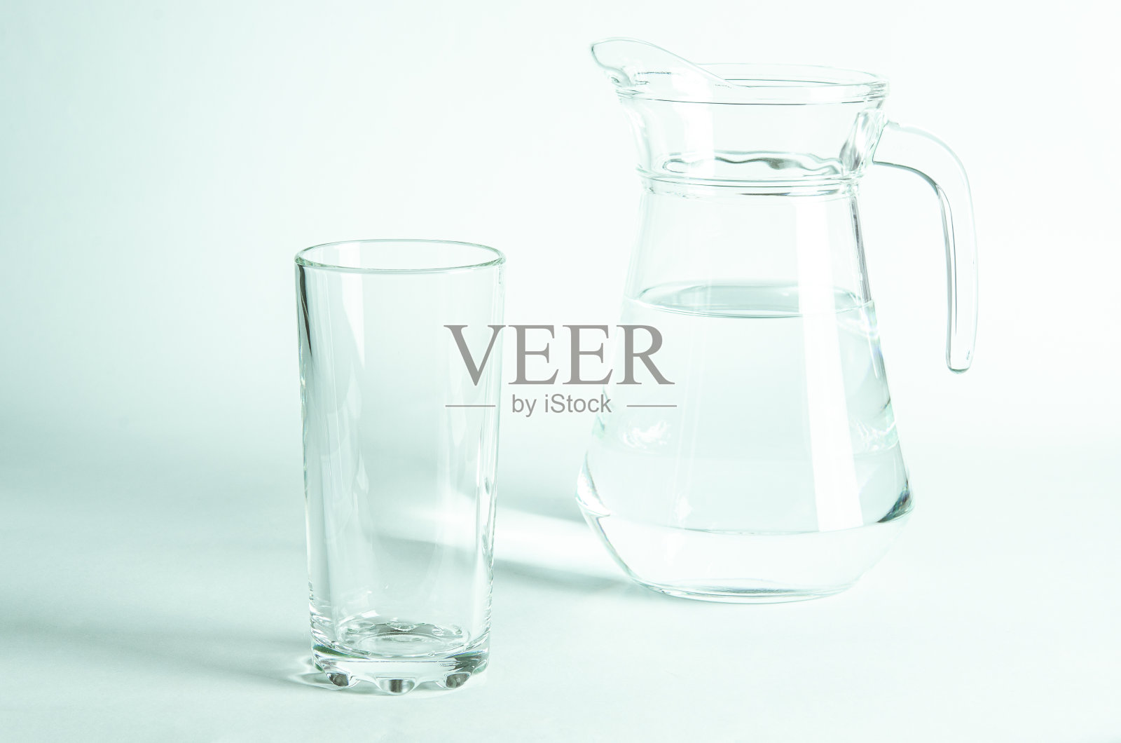 在白色的背景上，一个玻璃杯和水壶中纯净的水照片摄影图片