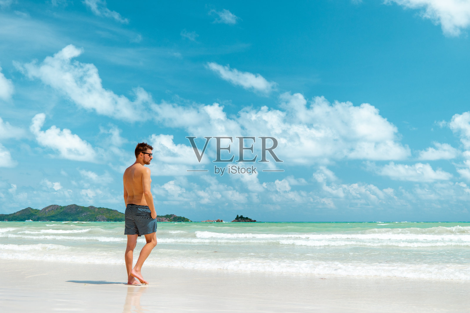 塞舌尔普拉兰岛热带海滩上的年轻人，棕榈树下的白色海滩，在热带度假的男人照片摄影图片