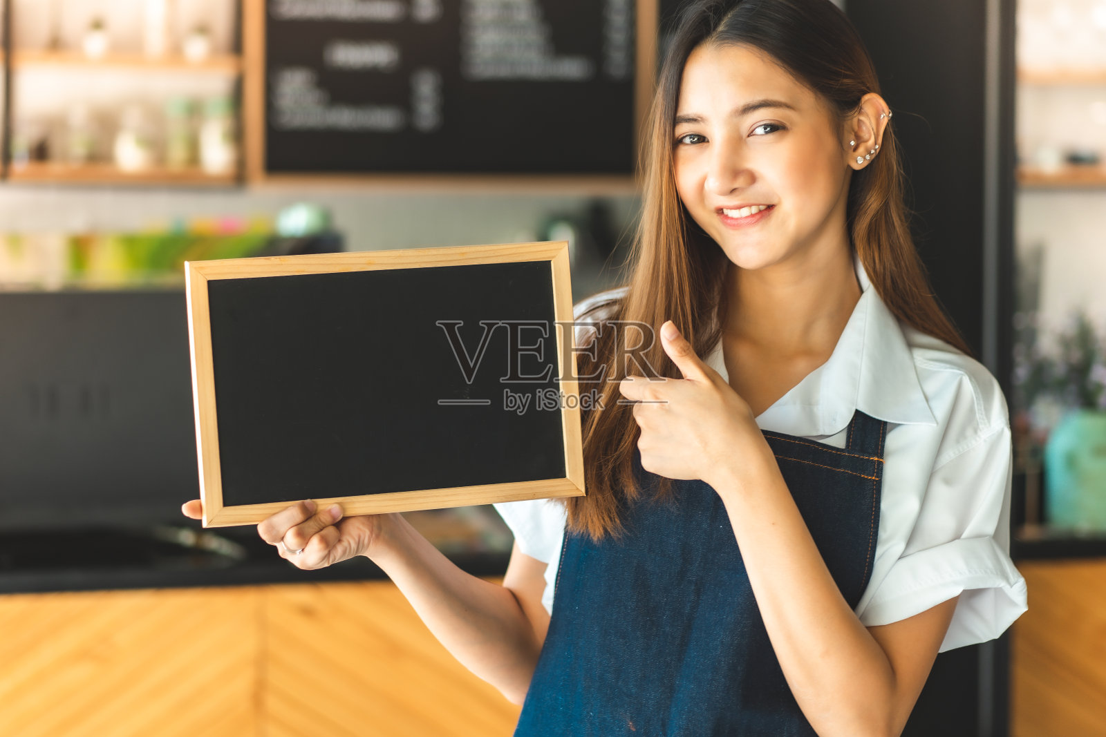 年轻漂亮的亚洲女招待双手交叉站在餐厅里。咖啡企业主的概念。穿着围裙的咖啡师在咖啡店柜台对着镜头微笑照片摄影图片