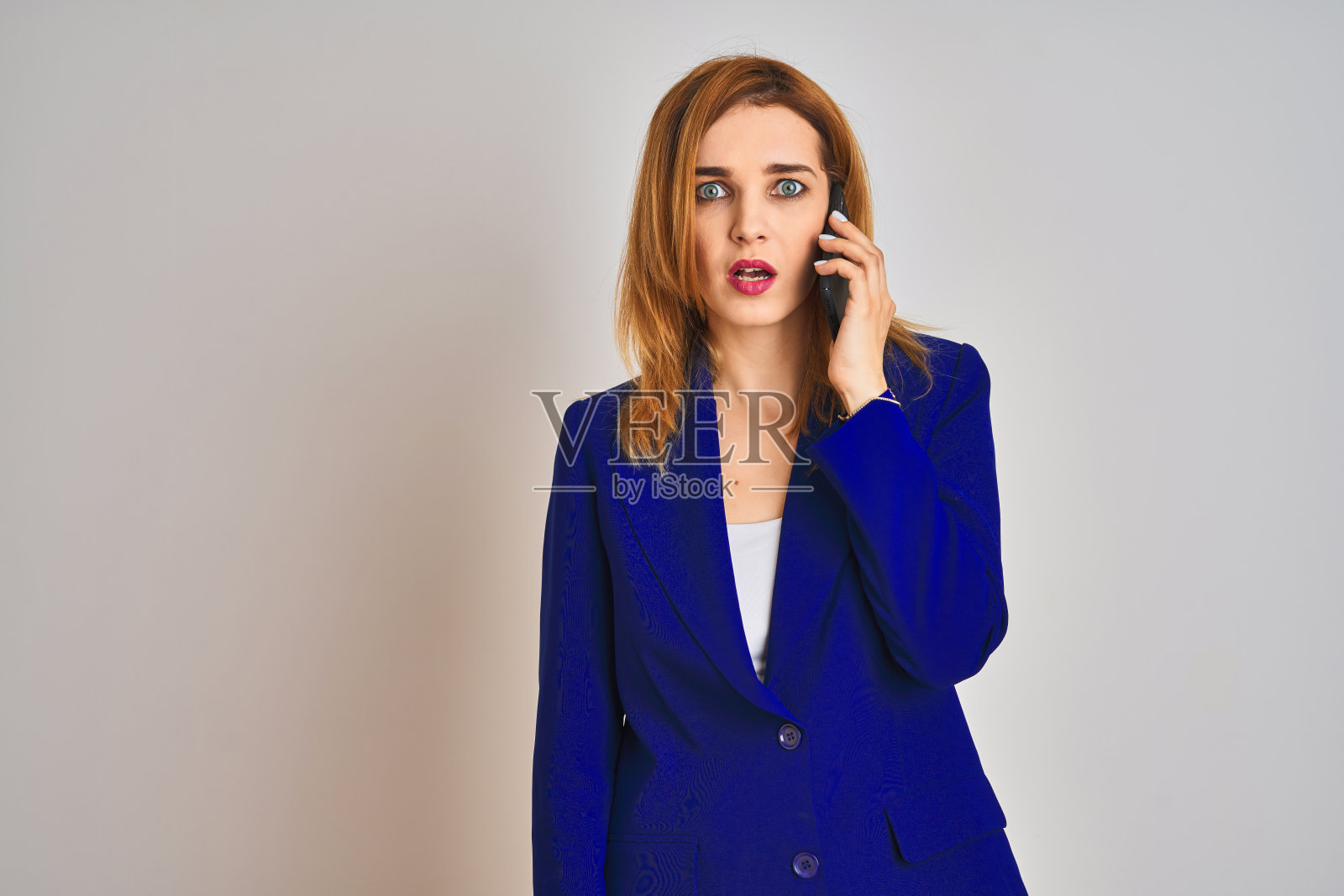 在隔离背景下打电话的年轻优雅的白人女商人，面带惊讶的表情，感到震惊、害怕和兴奋照片摄影图片