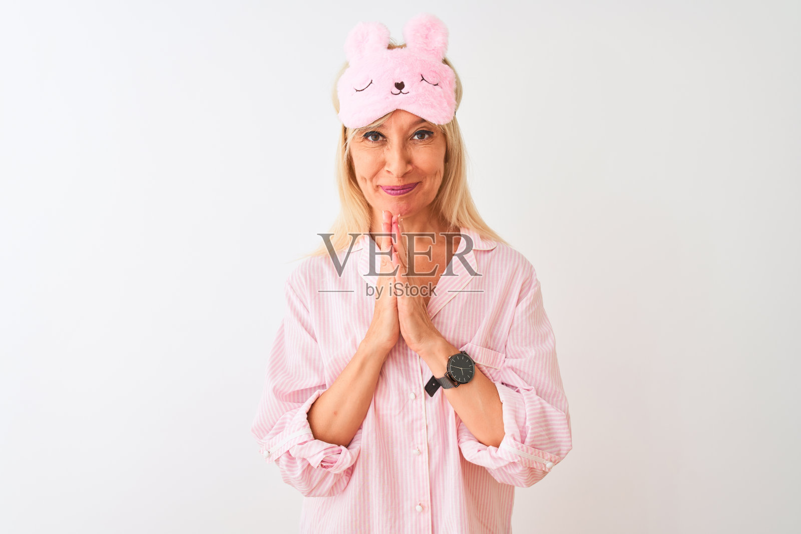 戴着睡眠眼罩和睡衣的中年妇女在白色背景前祈祷，请求原谅照片摄影图片