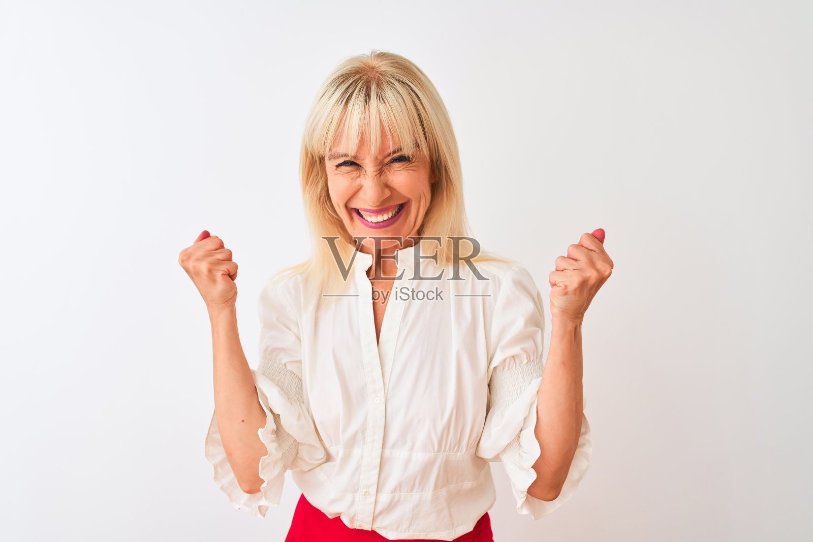 中年女商人穿着优雅的衬衫站在白色背景前，非常高兴和兴奋地做出胜利者的姿势，举起双臂，微笑着尖叫着庆祝成功照片摄影图片