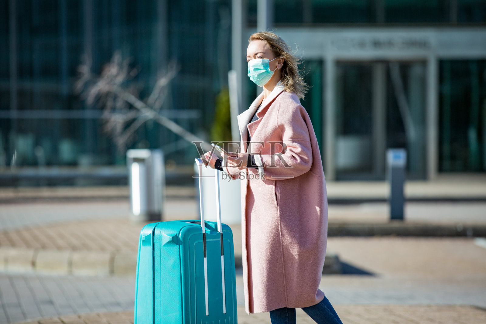 戴防护口罩的女人在机场入口处手持智能手机和大行李箱照片摄影图片