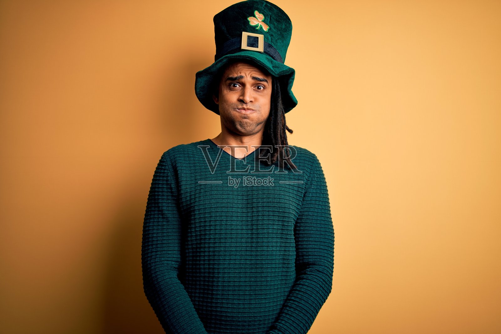 戴着三叶草绿色帽子的年轻非裔美国男子庆祝圣帕特里克节，鼓起脸颊，做出滑稽的表情。嘴巴里充满了空气，疯狂的表情。照片摄影图片