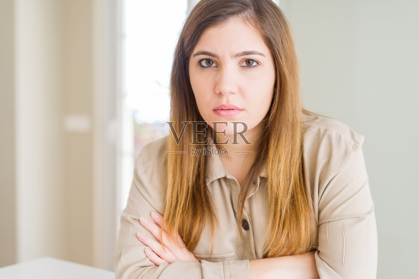 年轻女子在家中持怀疑和紧张态度，双臂交叉表示不赞成照片摄影图片