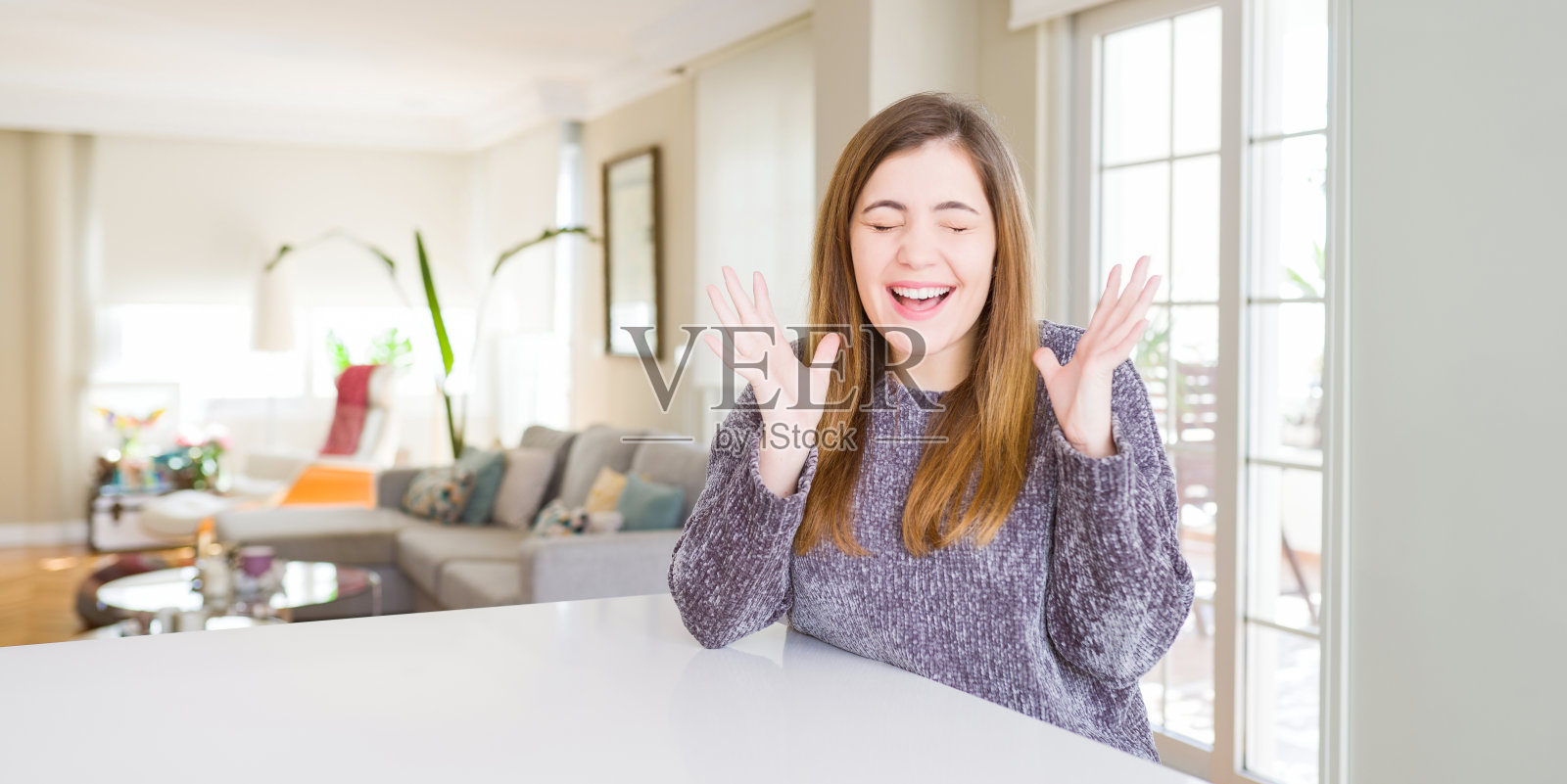 年轻女子在家中举起双臂，闭着眼睛尖叫，庆祝成功照片摄影图片