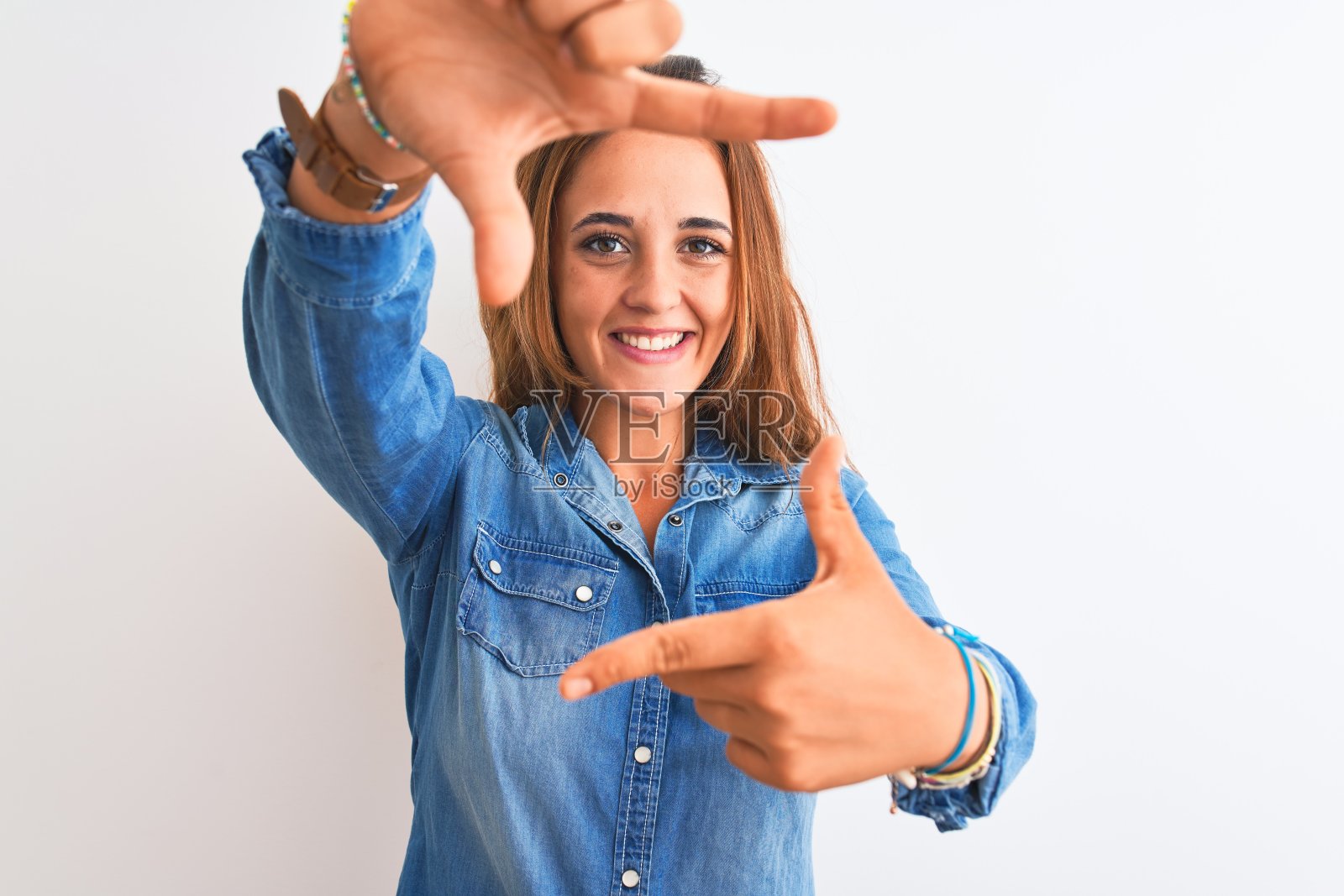 年轻的红发女子穿着牛仔夹克站在孤立的背景微笑与手和手指框架与快乐的脸。创意和摄影概念。照片摄影图片