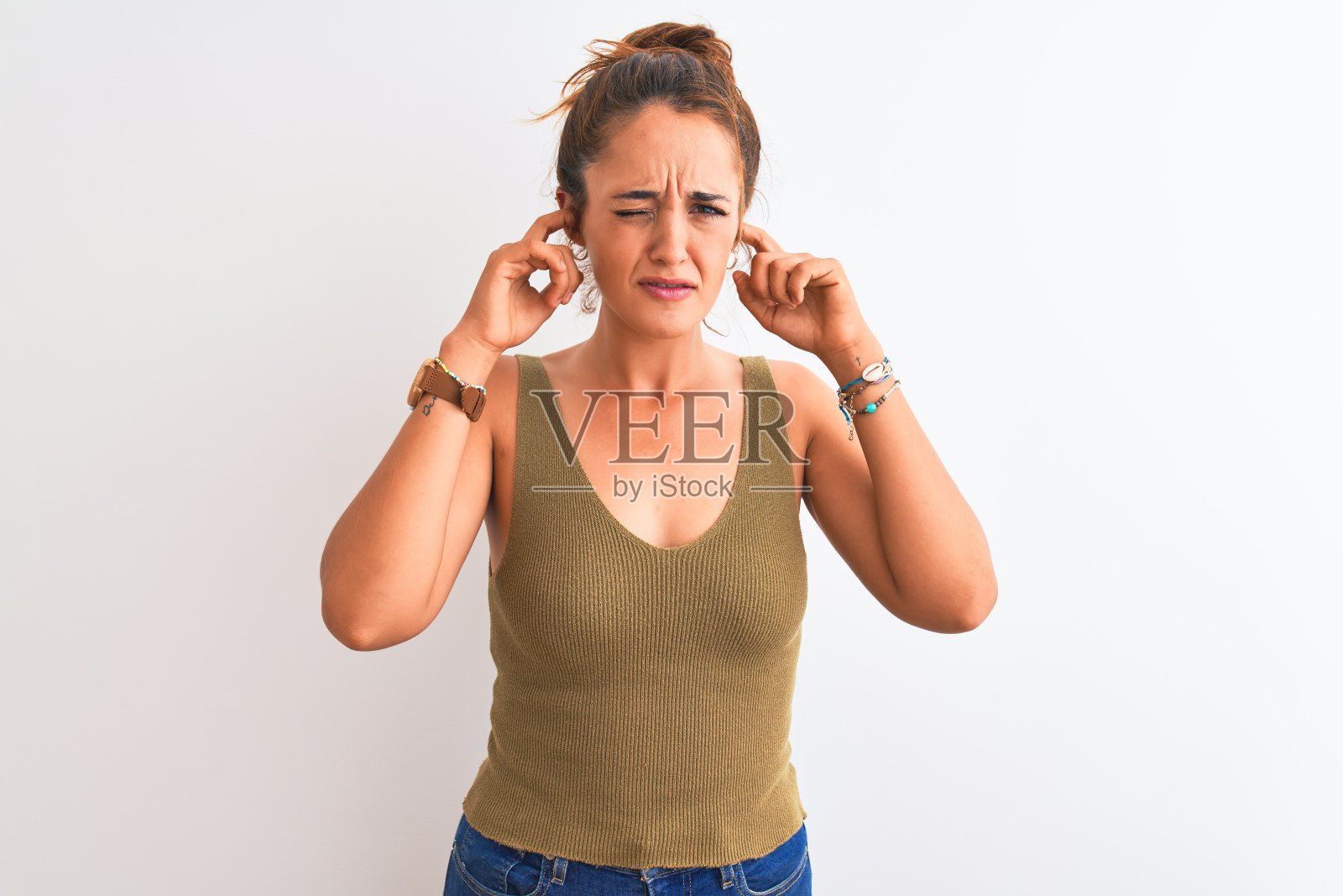 年轻的红发女人戴着一个发髻在孤立的背景掩盖耳朵与手指与烦恼的表情噪音的音乐。聋的概念。照片摄影图片