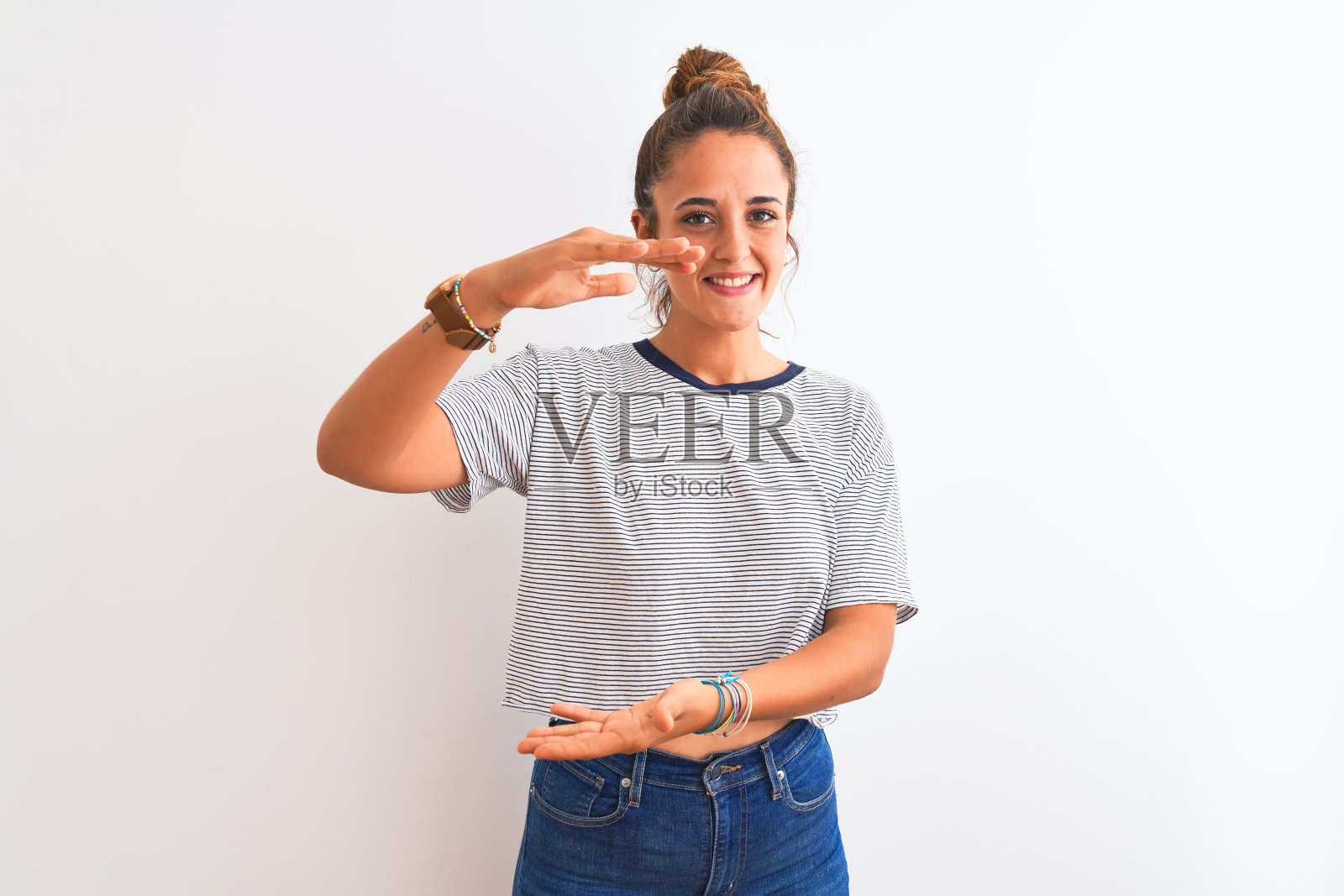 年轻的红发现代女性，在孤立的背景上梳着一个发髻，用手比划着大大的尺寸符号。看着镜头微笑。测量的概念。照片摄影图片