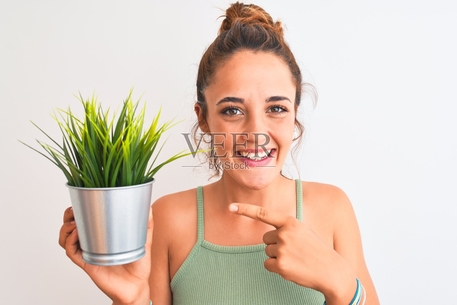 年轻的红发女子手持花盆越过孤立的背景，非常高兴地用手和手指指着照片摄影图片