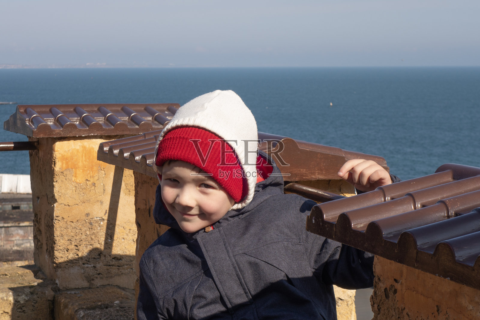 一个4岁的男孩在一个以大海为背景的古老堡垒里摆姿势。照片摄影图片