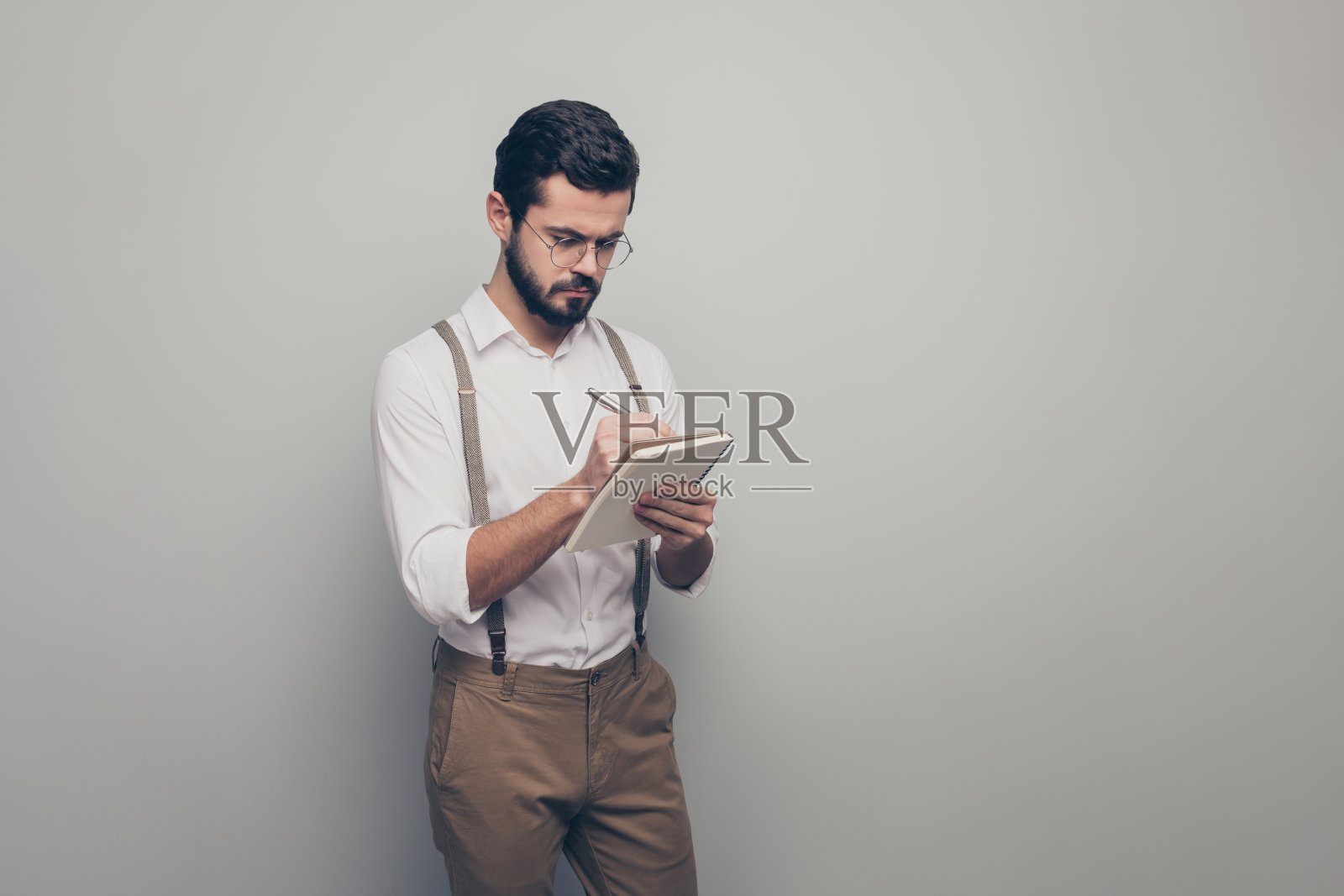 肖像集中的男子阳刚野蛮代理人写抄写笔整理他的老板日常的一天穿白色棕色的裤子孤立在灰色的背景照片摄影图片