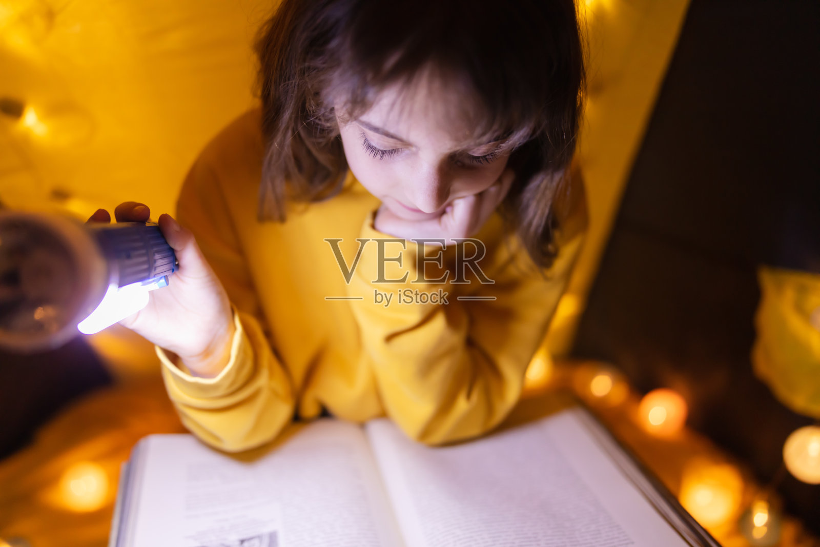 年轻的女孩子在家里用轻球做的起居室帐篷里阅读百科全书。照片摄影图片