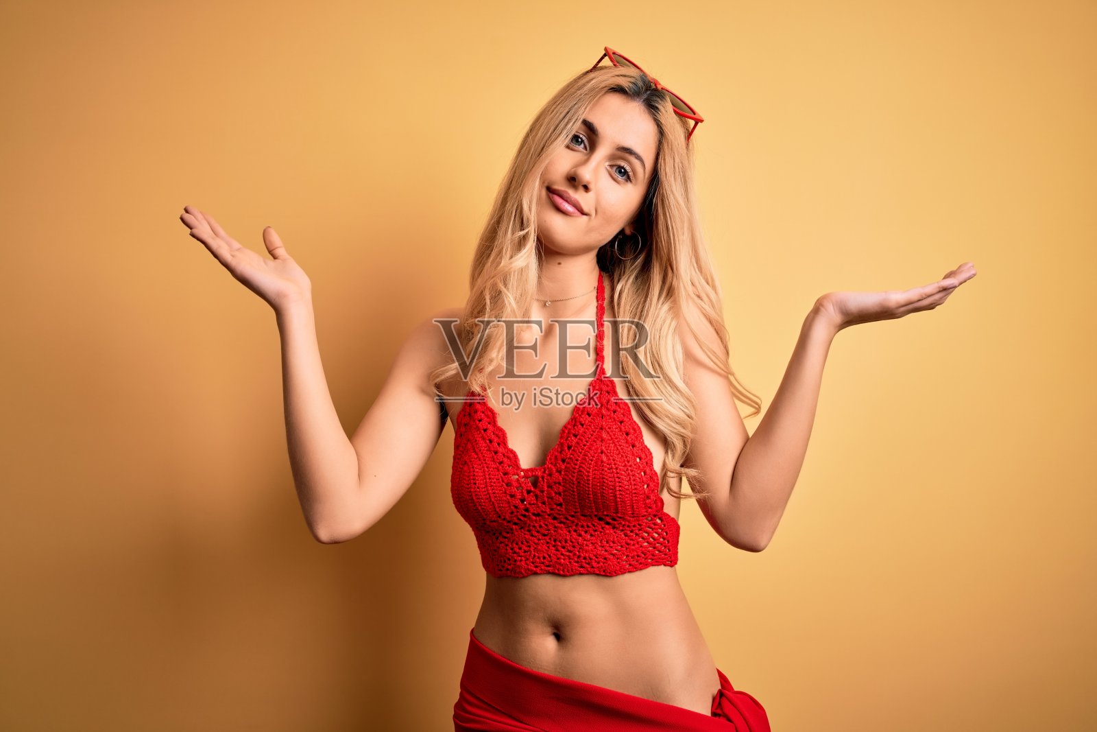 年轻美丽的金发女人度假穿比基尼在孤立的黄色背景愚蠢和困惑的表情与胳膊和手举起。怀疑的概念。照片摄影图片