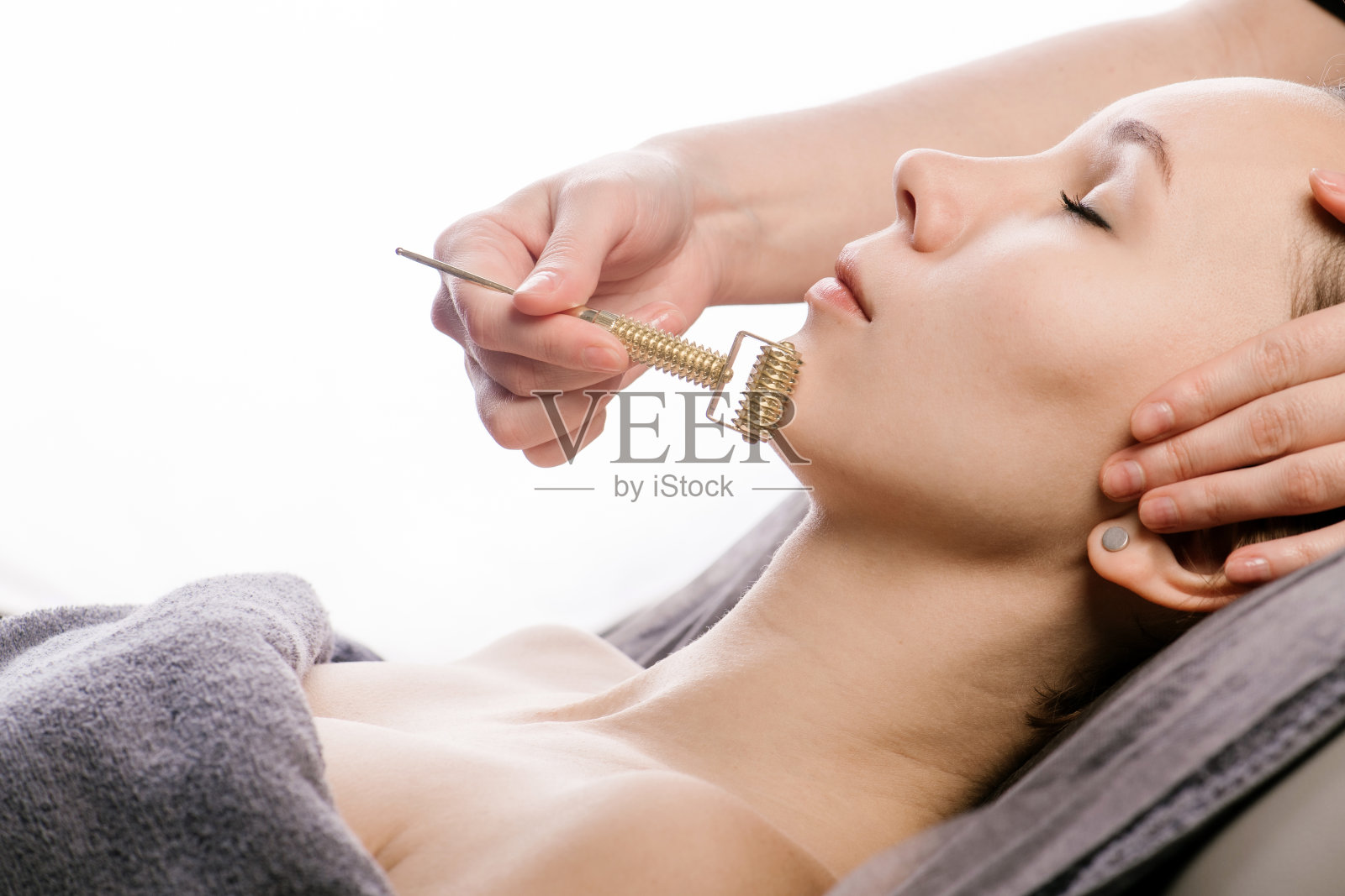 在美容院进行刮痧面部按摩时，面部滚轮滑过下巴的场景照片摄影图片