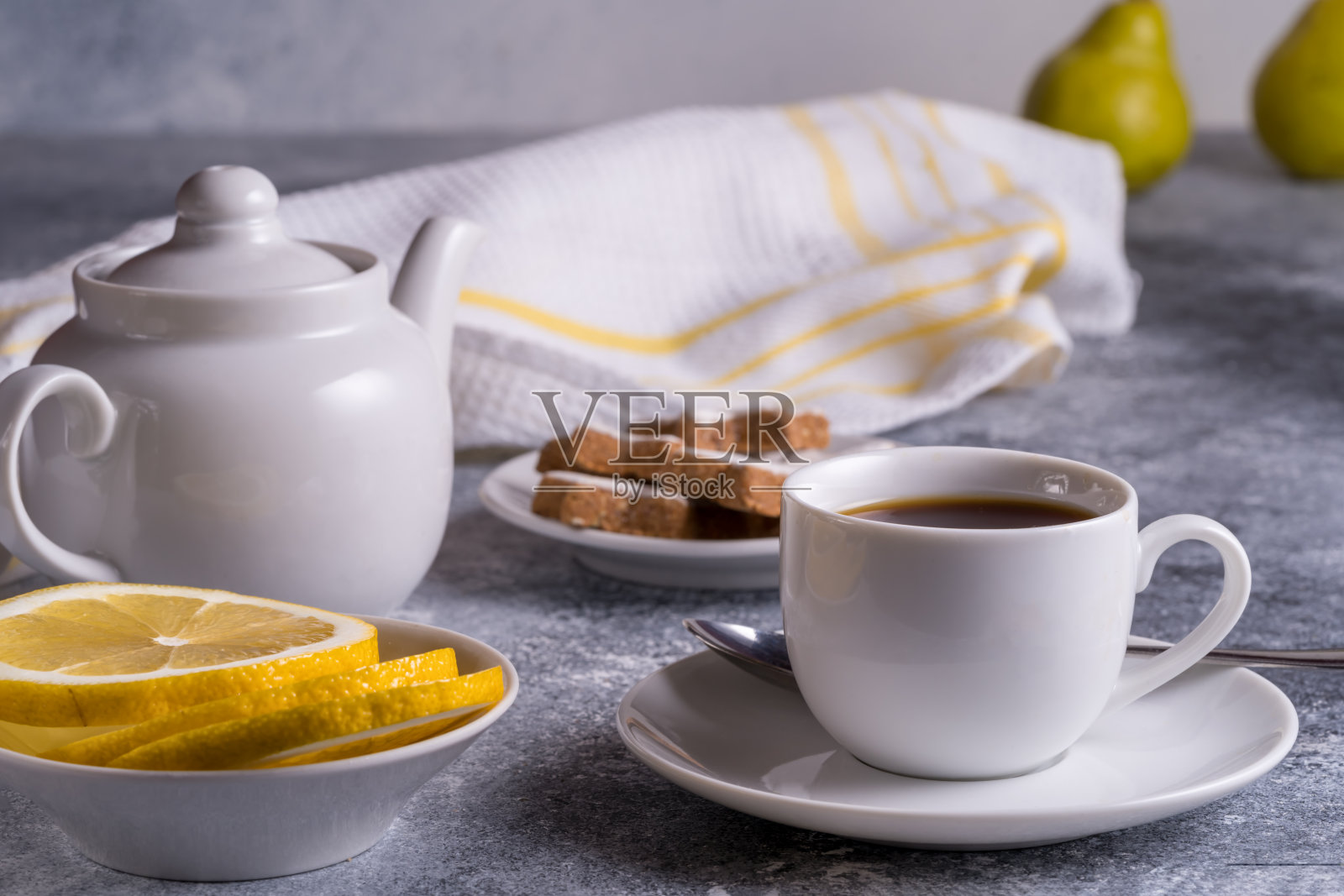 桌上放着茶杯、茶壶、蛋糕和柠檬，散景背景上模糊了梨子。照片摄影图片