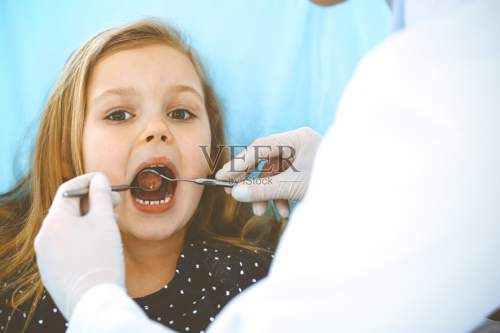 小女孩张大嘴巴坐在牙科椅上接受医生的口腔检查。拜访牙医的办公室。医学概念。健美的照片照片摄影图片