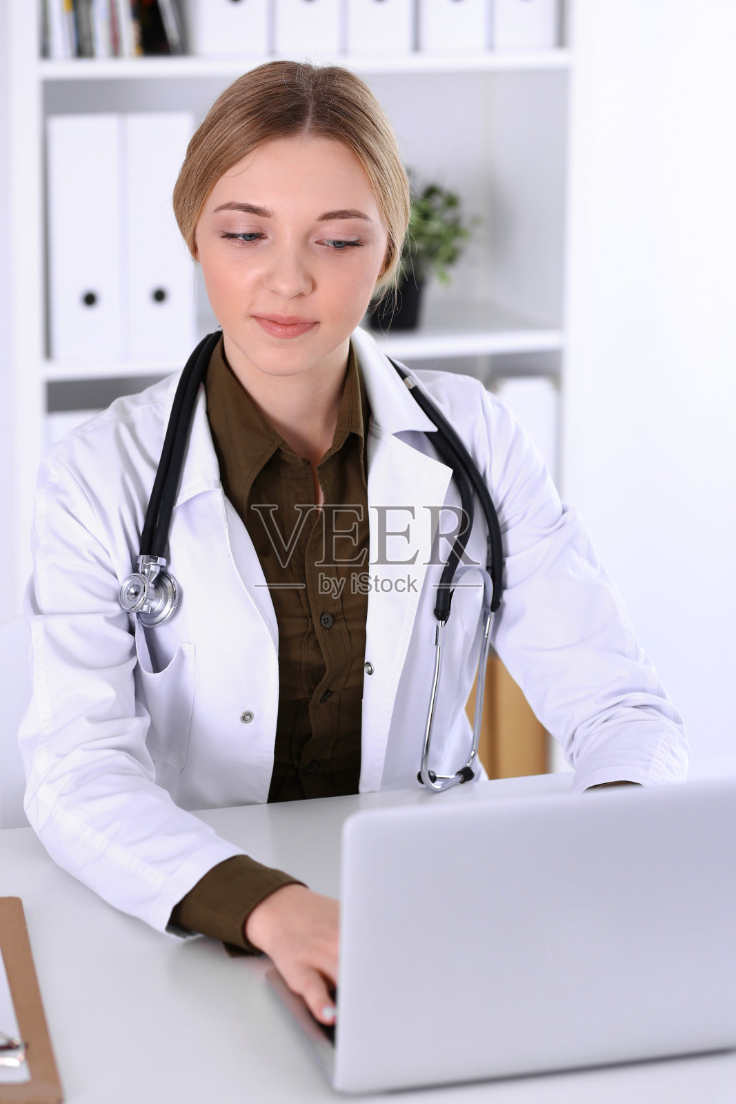 在医院工作的年轻女医生看着笔记本电脑显示器，医生控制药物病史记录和检查结果，医学和保健概念照片摄影图片