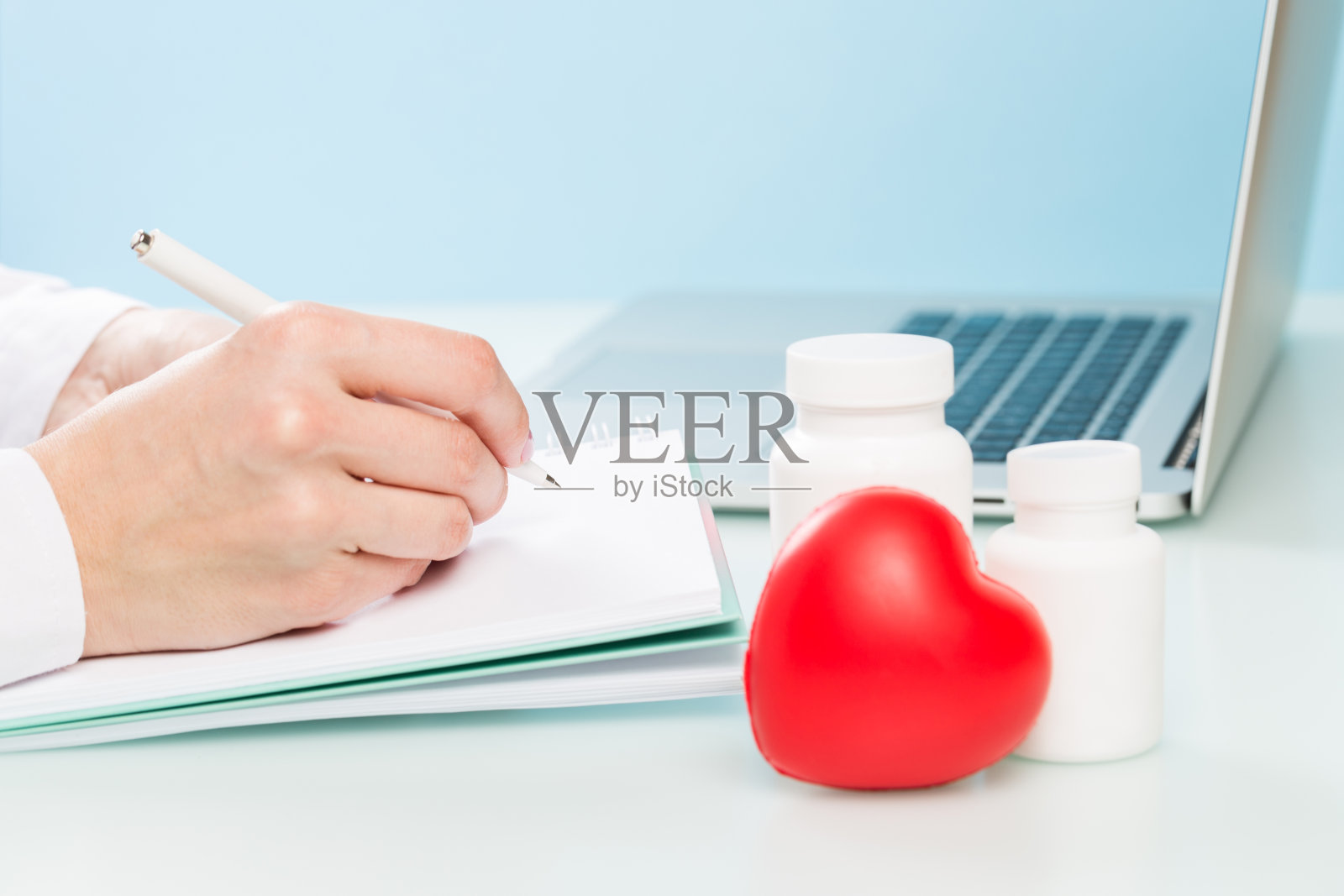 医生的手使用笔记本电脑，用钢笔在蓝色背景的纸上写字。医学理念，现代技术照片摄影图片