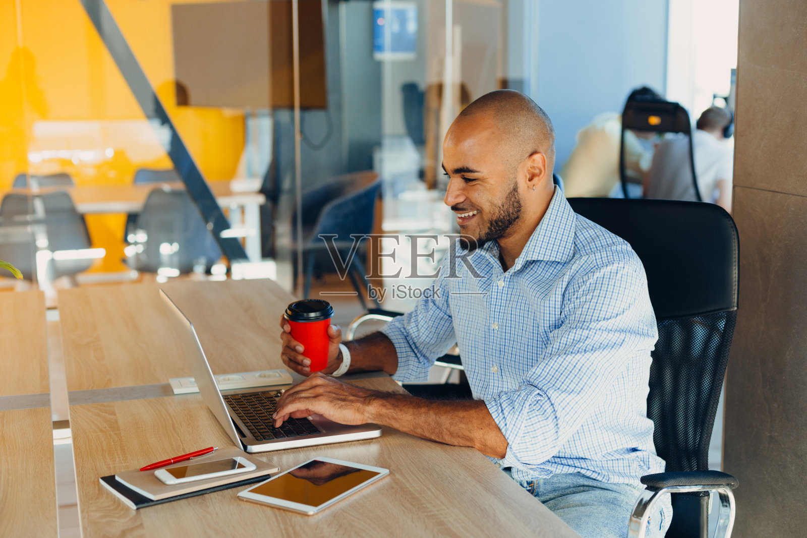 自信的年轻非裔美国商人坐在创业办公室里使用笔记本电脑和手机照片摄影图片