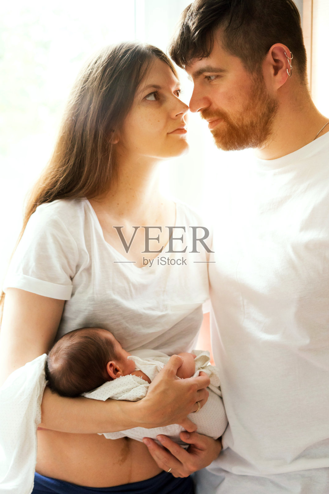 逆光下，父母与新生儿子在窗边照片摄影图片