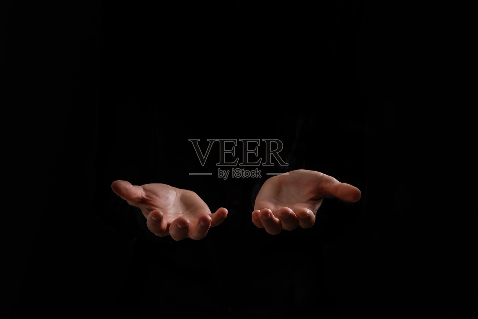 英俊男子坐在祈祷黑色的背景。他的双手在祈祷上帝的保佑。照片摄影图片