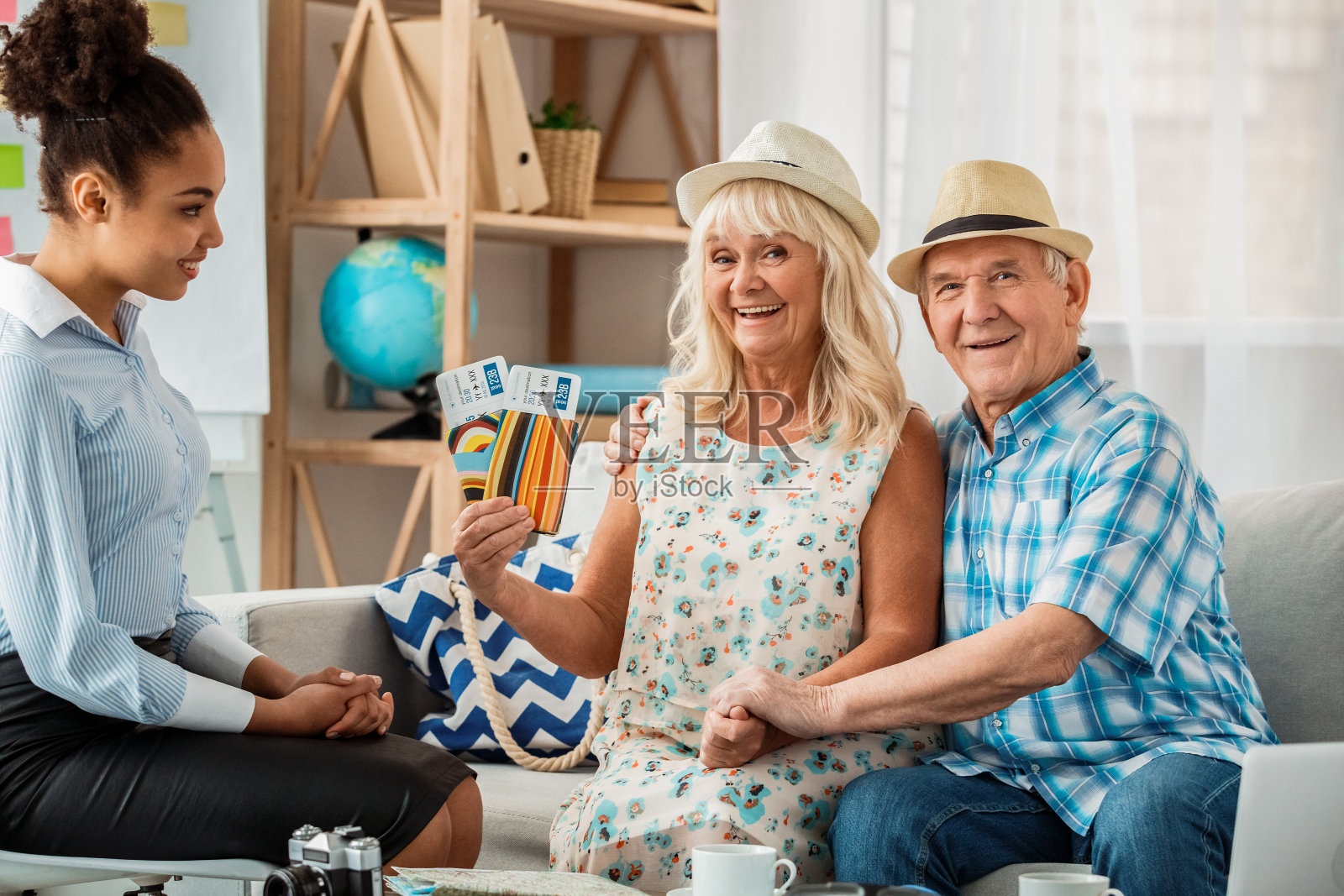 旅行社代理办公室的高级客户戴着沙滩帽，兴高采烈地拿着护照和机票照片摄影图片