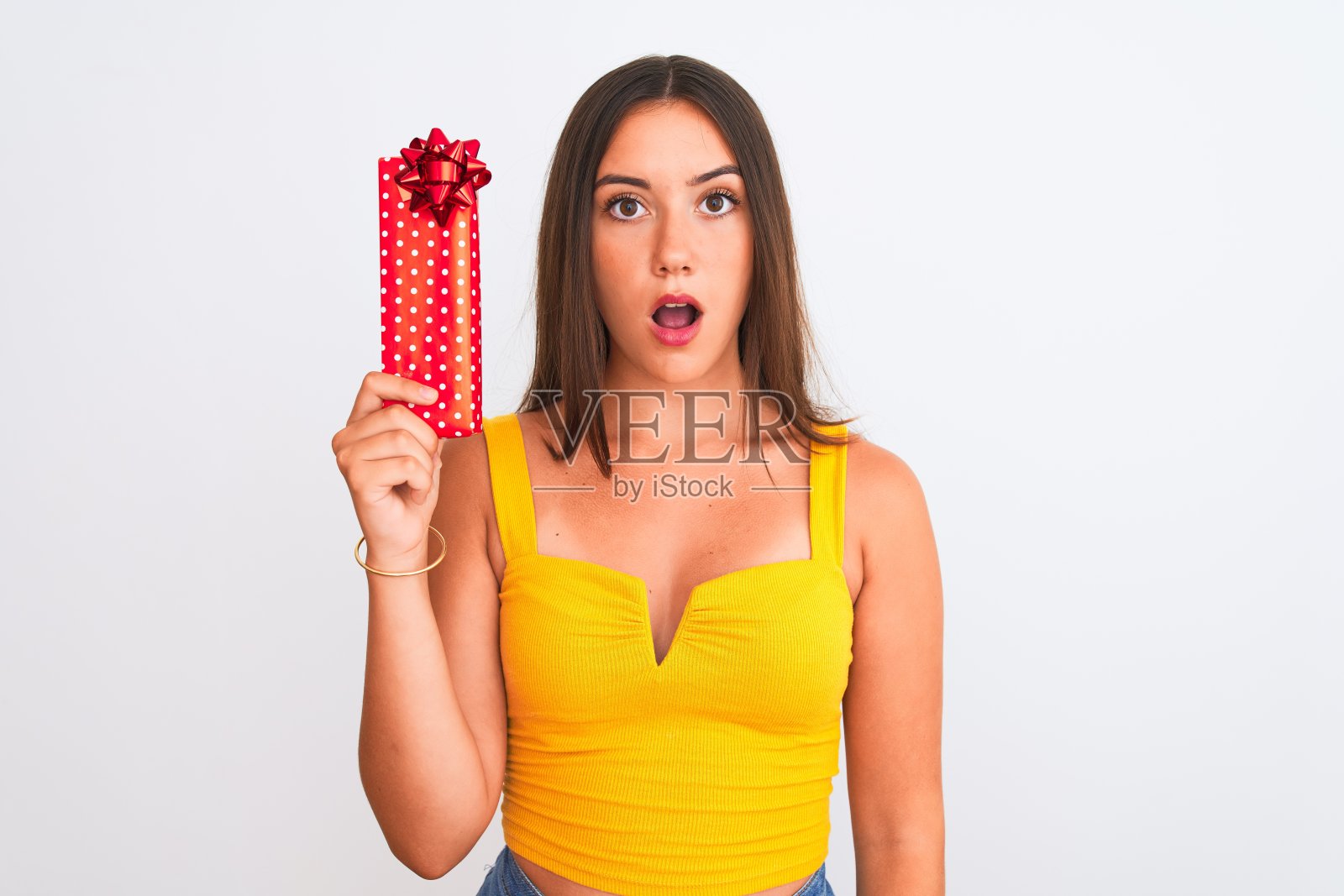 年轻美丽的女孩拿着生日礼物站在孤立的白色背景吓在震惊与惊喜的脸，害怕和兴奋与恐惧的表情照片摄影图片