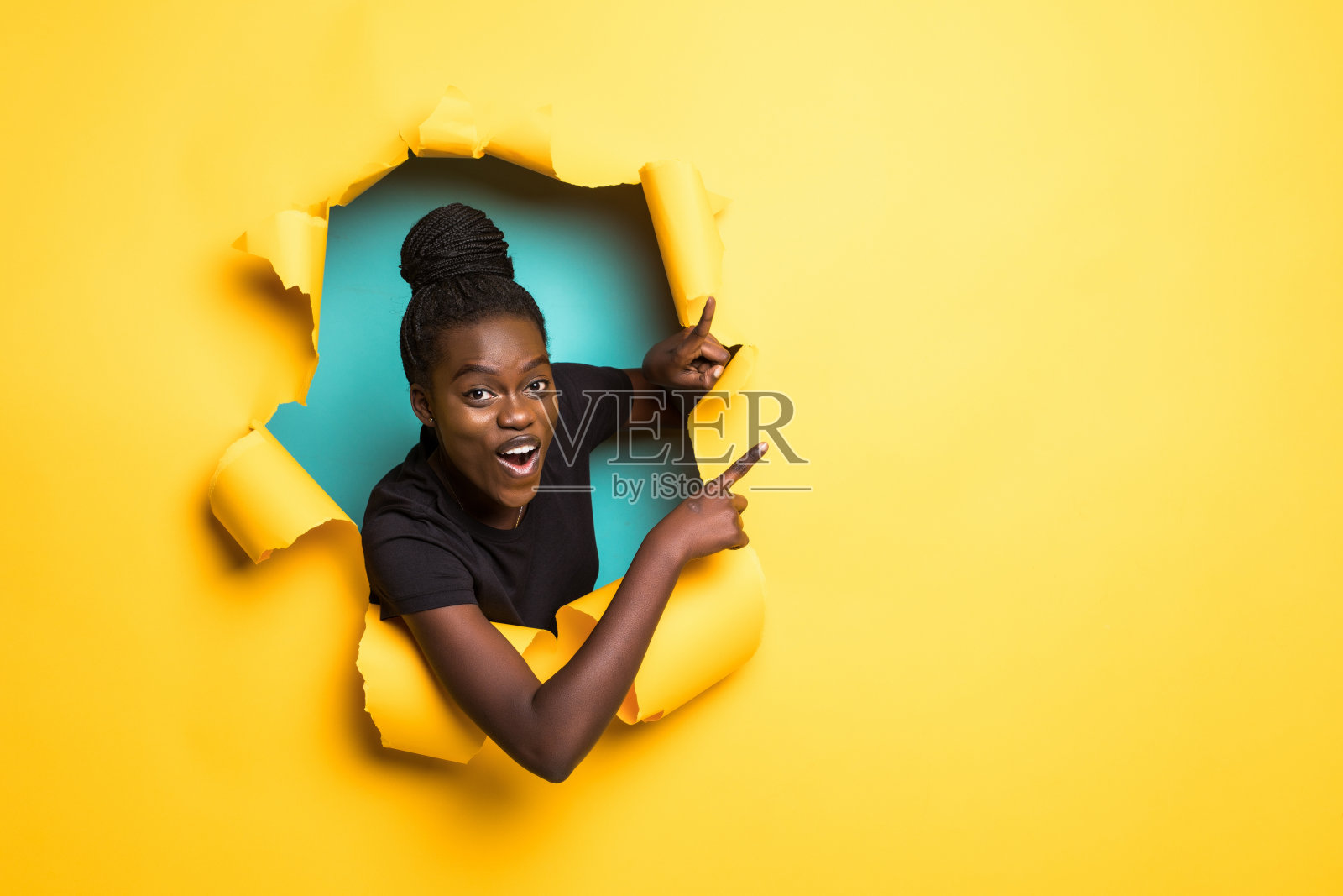 从黄色纸洞里指向侧面并摆姿势的年轻非洲裔女子照片摄影图片