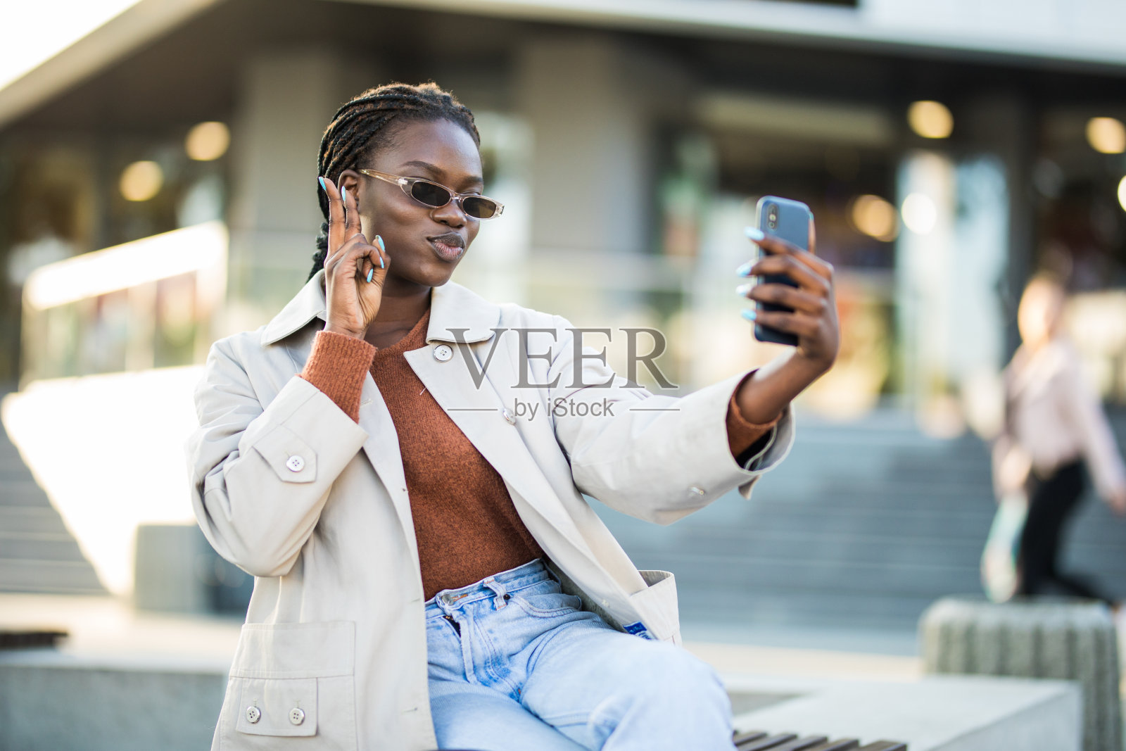 戴着耳机的非裔美国女性坐在长椅上用智能手机进行视频通话或自拍的肖像照片摄影图片