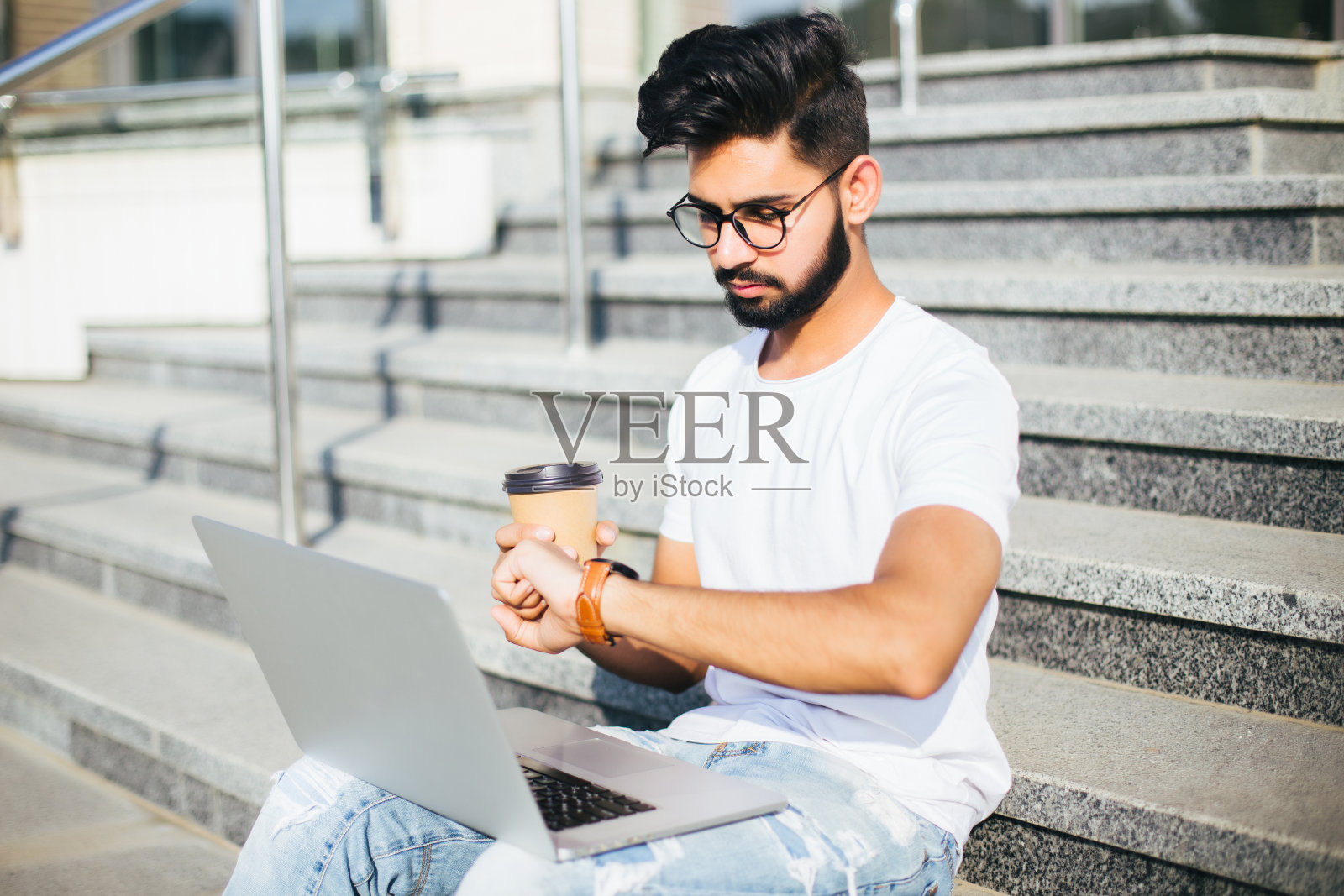 坐在户外楼梯上工作看手表的印度英俊年轻人照片摄影图片