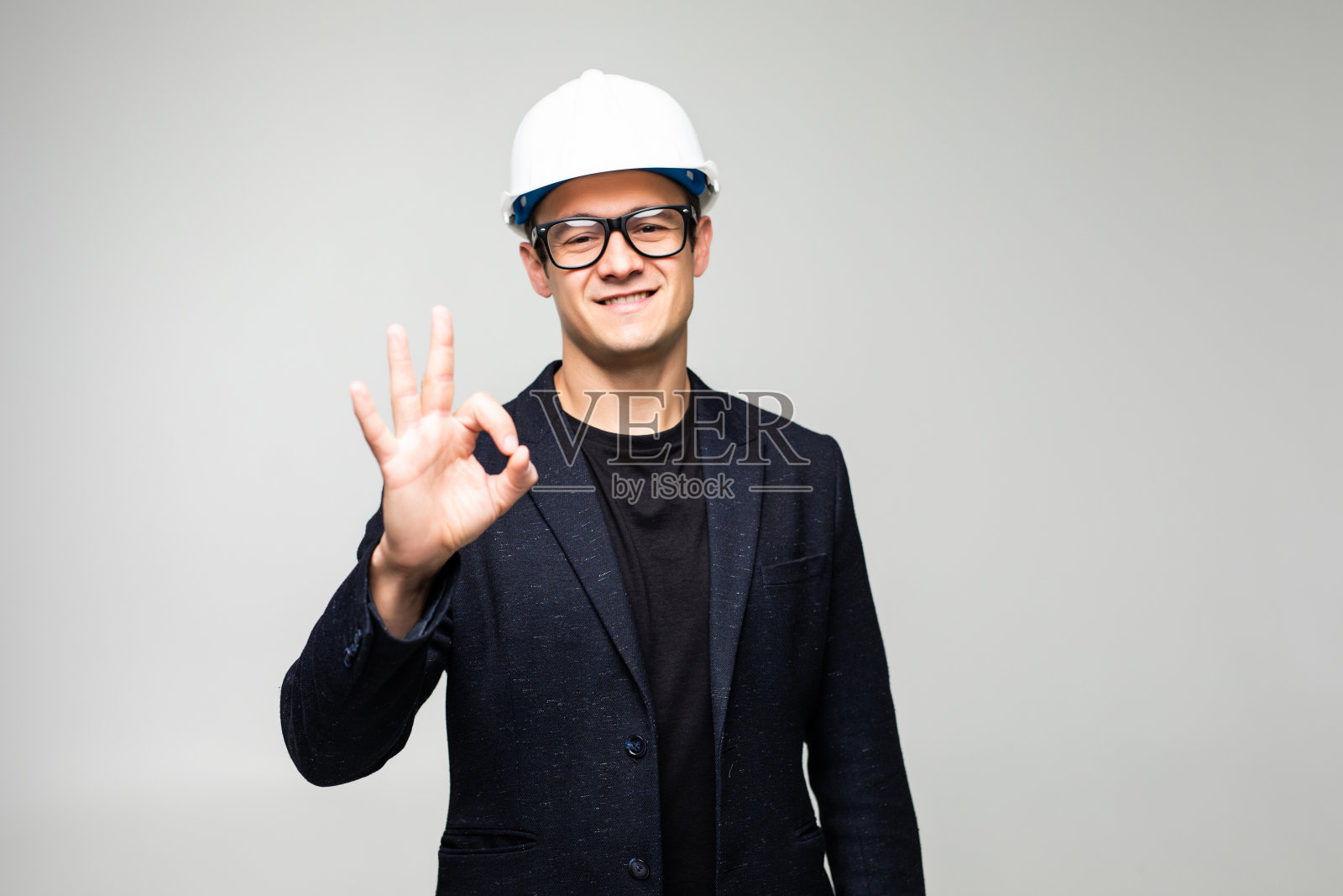 戴着施工安全帽，用手和手指做出OK手势的积极乐观的年轻商人。成功的表达。照片摄影图片
