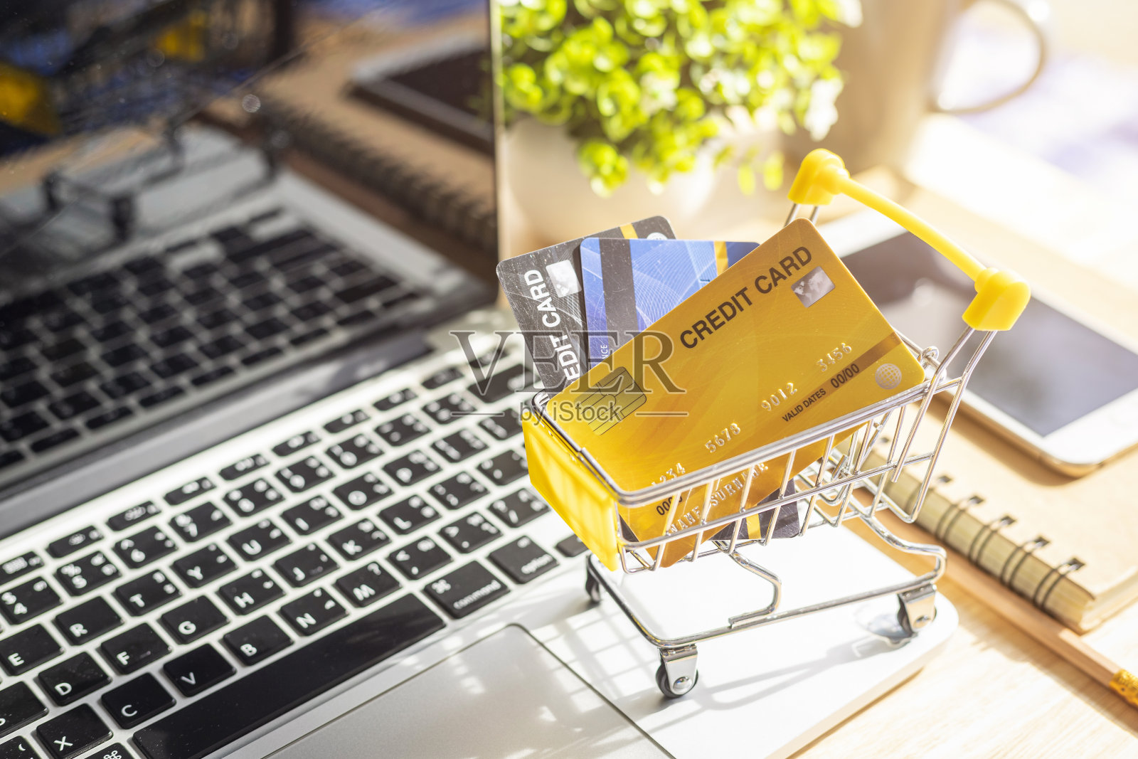 信用卡在购物车与笔记本电脑，笔记本电脑，花盆树，智能手机在木制背景，网上银行概念，顶视图办公室桌子。照片摄影图片