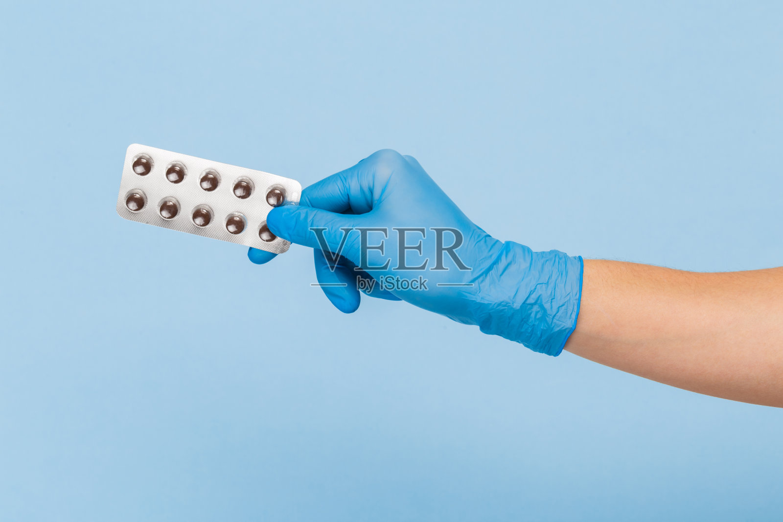 医生的手戴着蓝色医用手套，蓝色背景上有一个药丸泡。治疗照片摄影图片