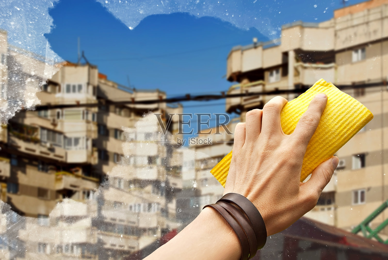 那个人用一条黄色的毛巾擦窗户。手关闭。城市的街道和外面的房子。肮脏的窗户锐利。照片摄影图片