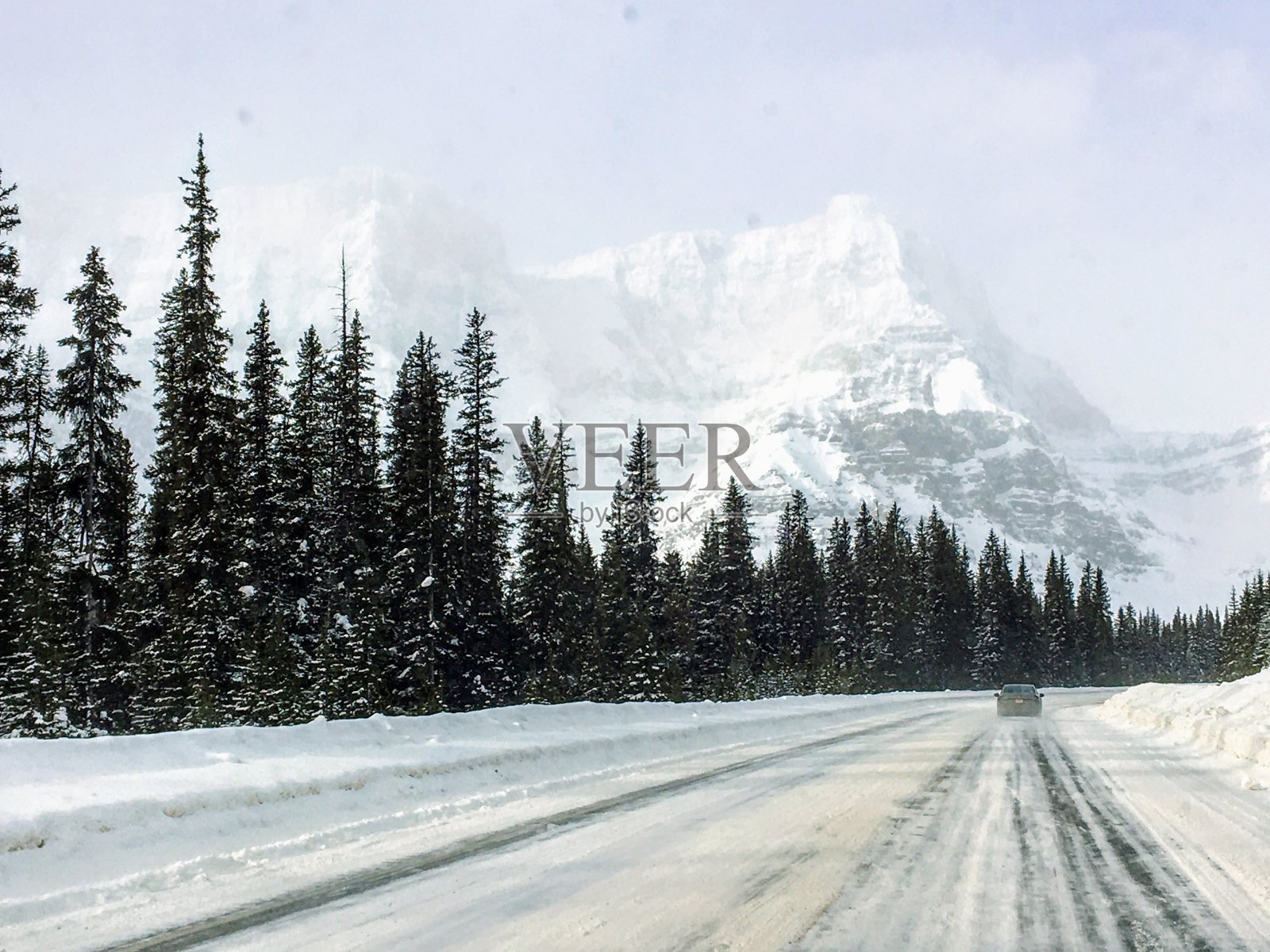 在加拿大阿尔伯塔省，一辆汽车在空旷的高速公路上行驶，后面是一座巨大的雪山照片摄影图片