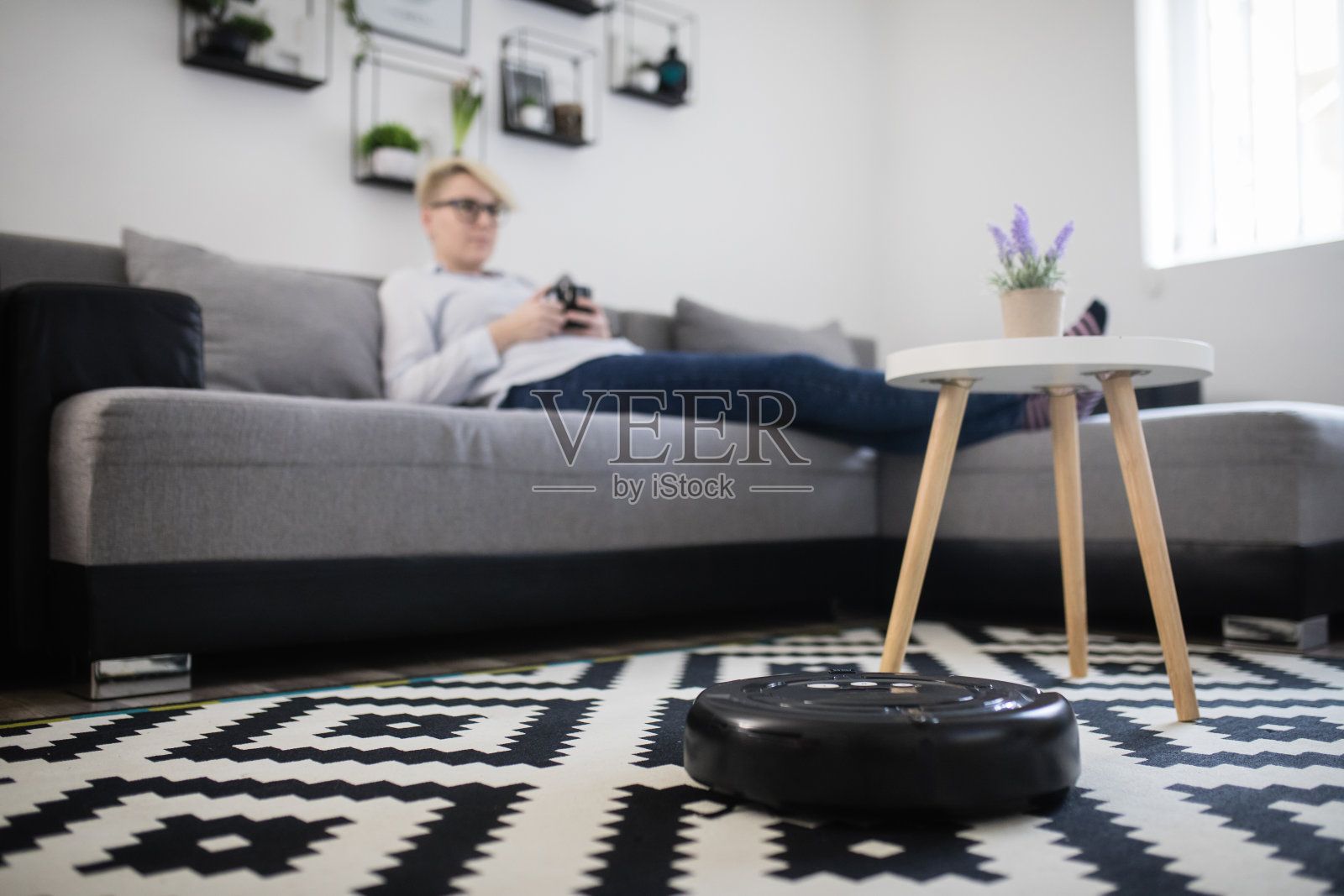 女士在沙发上休息，扫地机器人在清洁房间照片摄影图片