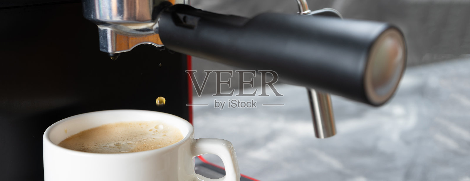 最后一滴咖啡从滤嘴掉到咖啡杯里。红色的咖啡机将热的意式浓缩咖啡倒入一个白色的杯子里。照片摄影图片