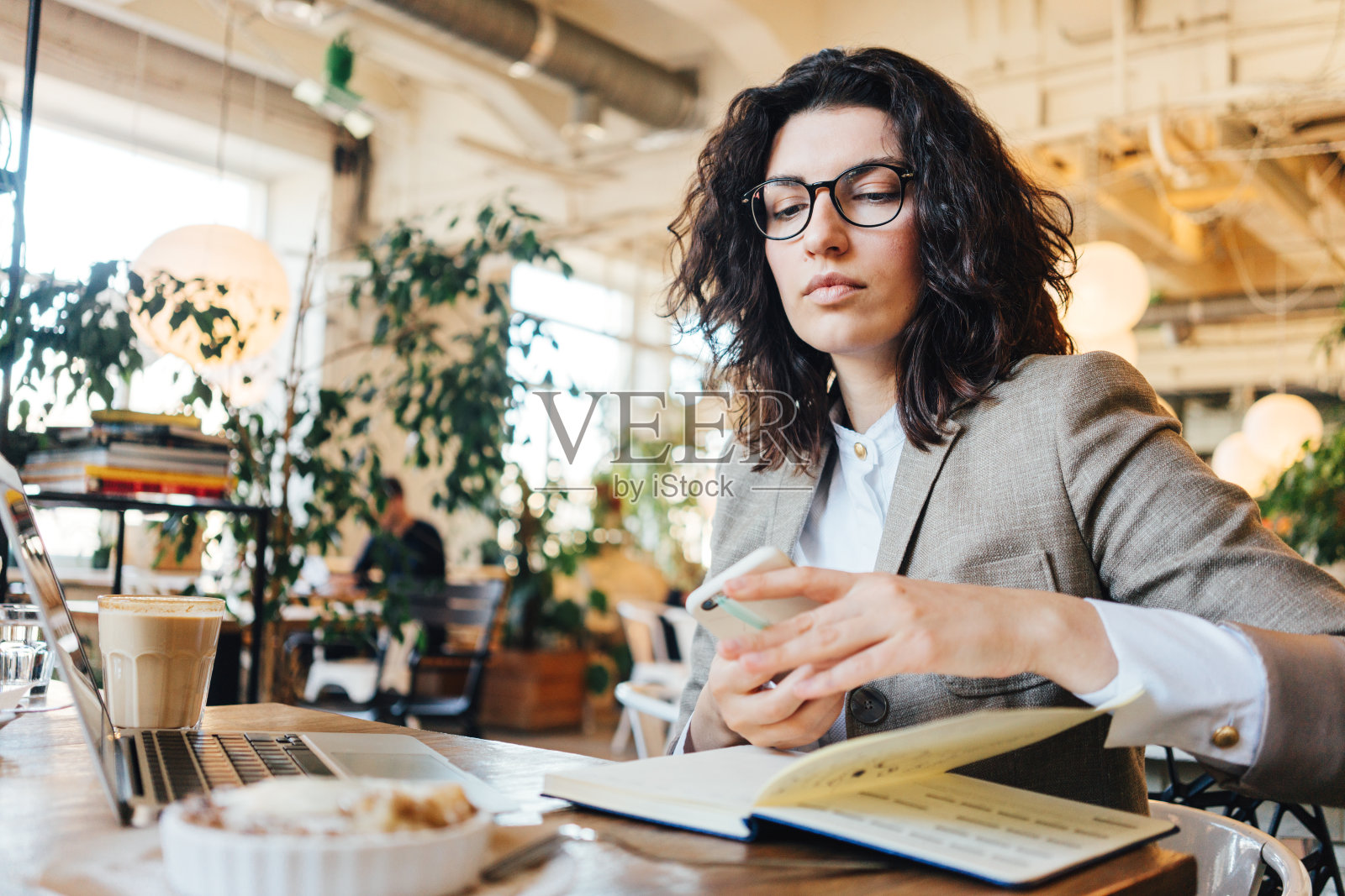 戴眼镜的卷发女人坐在咖啡馆里用手机工作照片摄影图片