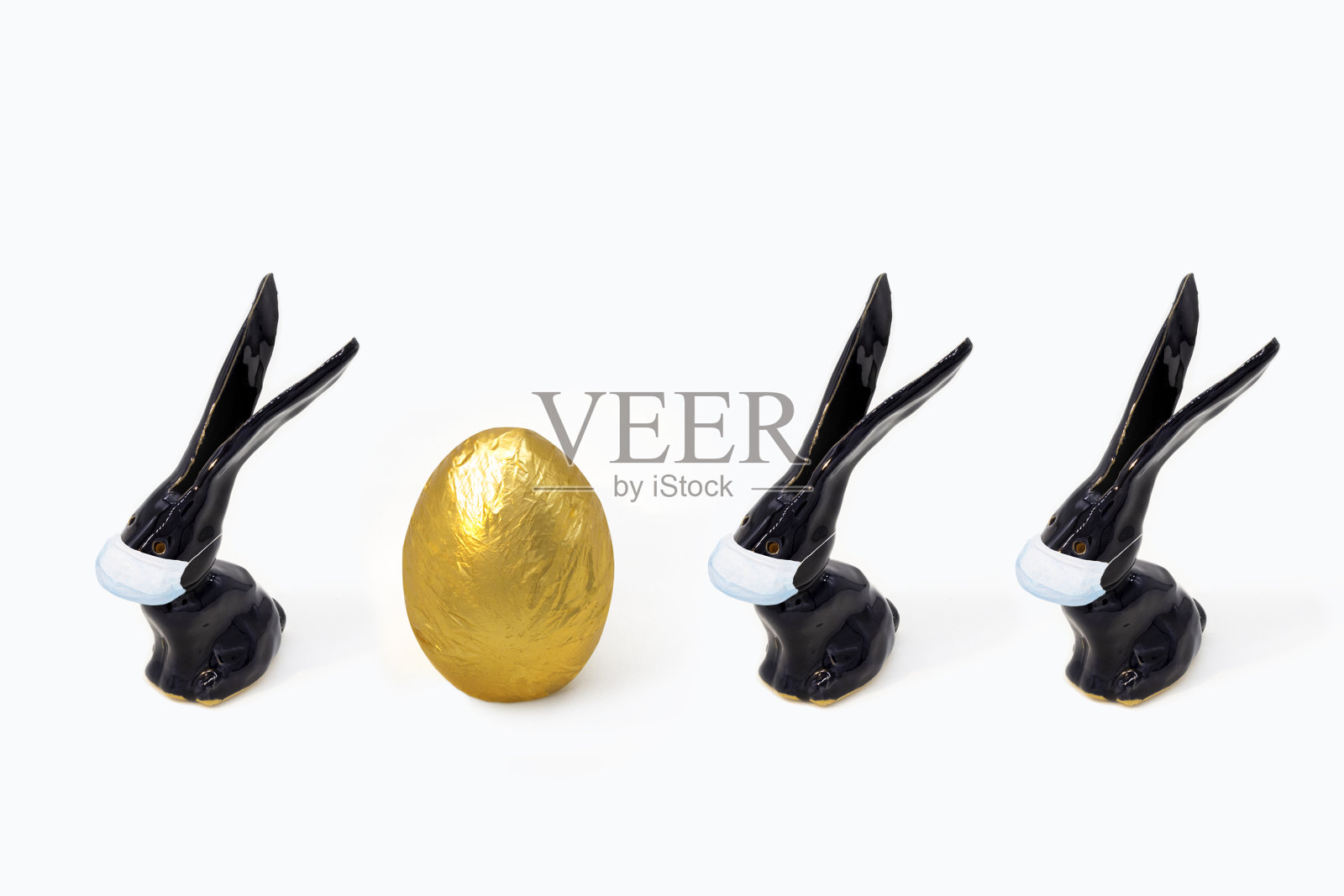 时髦的复活节装饰集-金色的蛋和黑色的兔子与病毒面具在白色的背景。复活节贺卡与副本空间。极简风格的冠状病毒防护概念。照片摄影图片