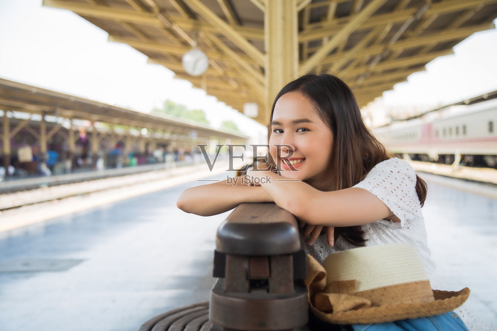 近距离拍摄美丽的年轻亚洲女子在白色的裙子坐在木凳上把她的下巴放在她的胳膊上，微笑着看着镜头照片摄影图片