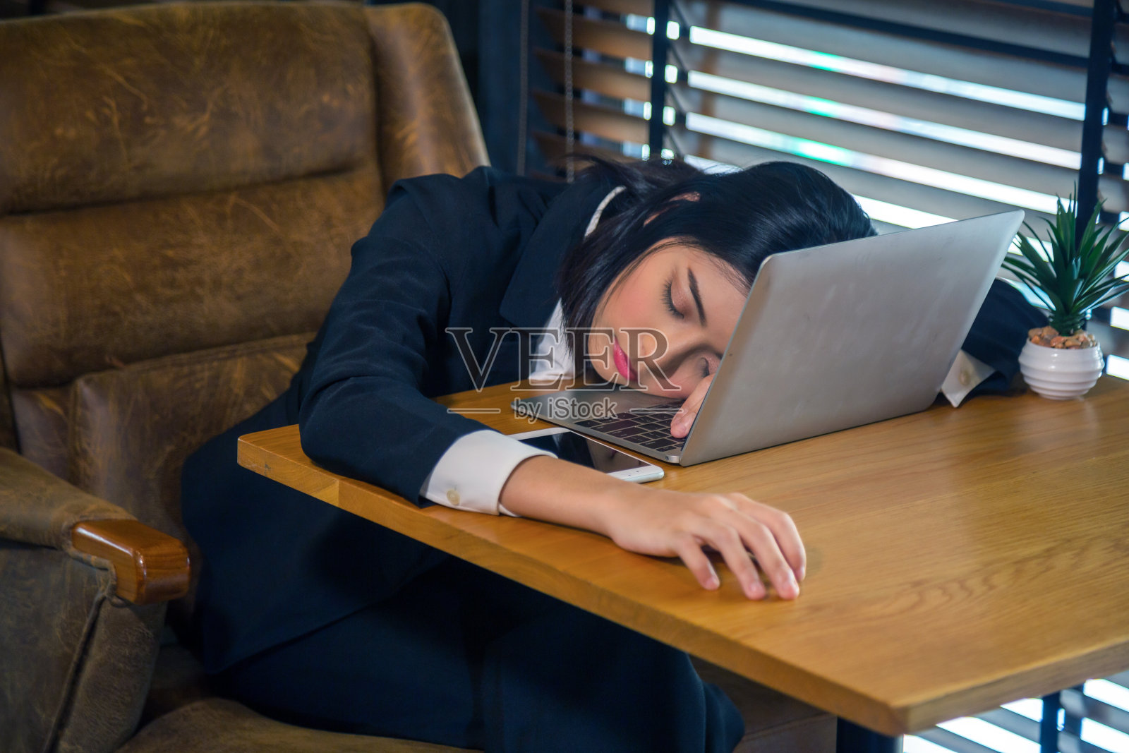 一名穿着正装的亚洲女子正睡在笔记本电脑上。照片摄影图片