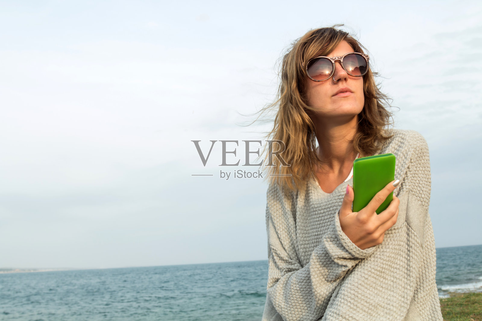 一个年轻女人在沙滩上玩手机。照片摄影图片