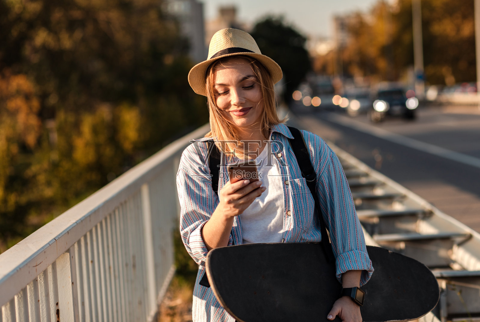 在城市里微笑的女孩，手拿滑板和手机照片摄影图片